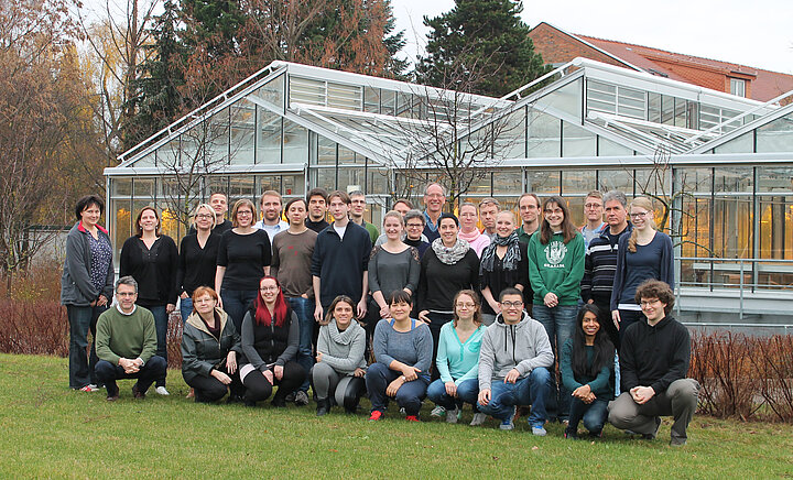 A group photo of about 30 people in front of a greenhouse.